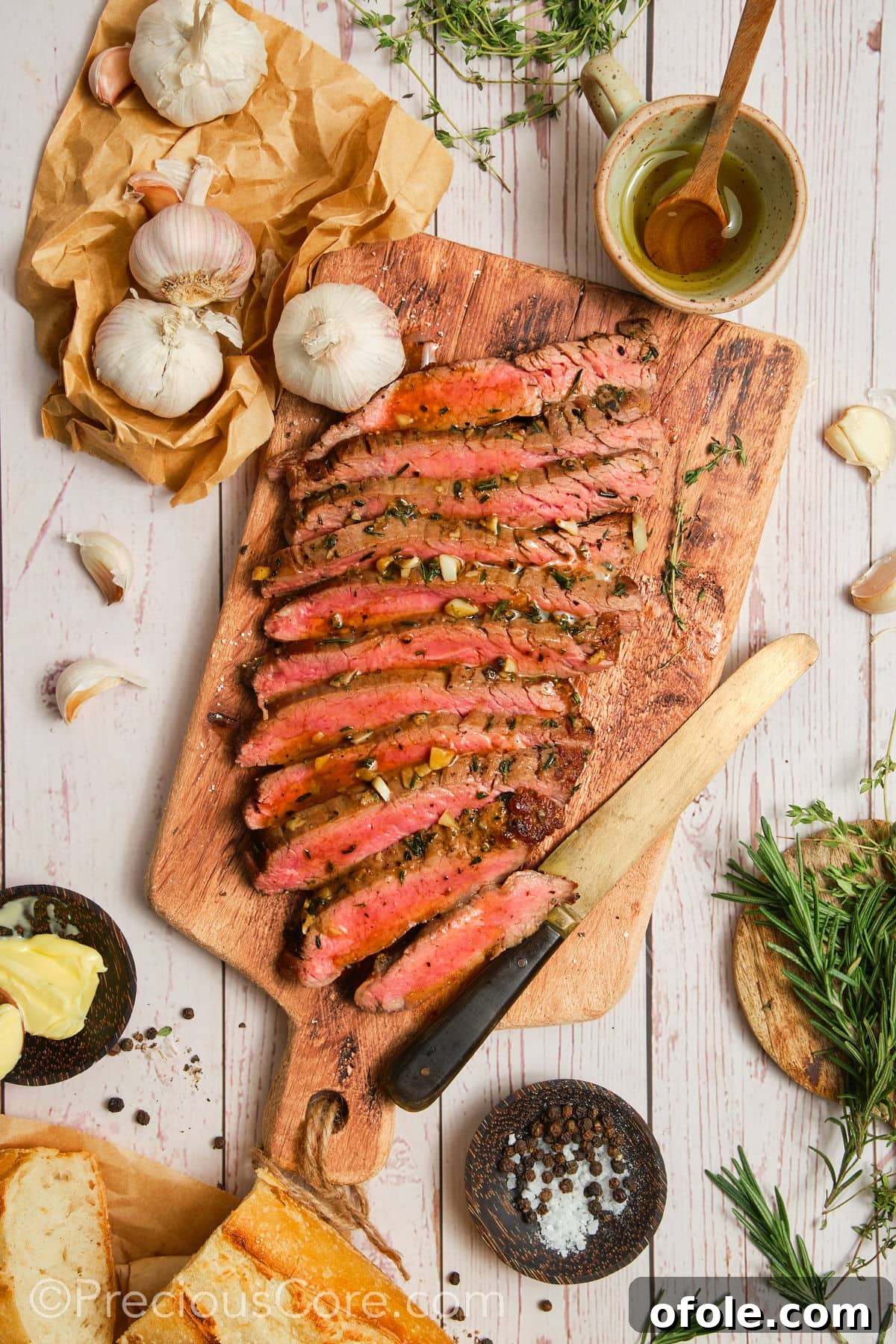 Cooked flank steak surrounded by fresh ingredients like herbs, garlic, and butter, ready for plating.