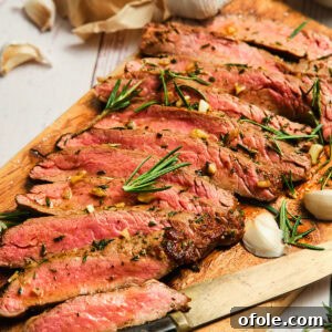 Sliced pan seared flank steak on a cutting board, garnished with fresh herbs.
