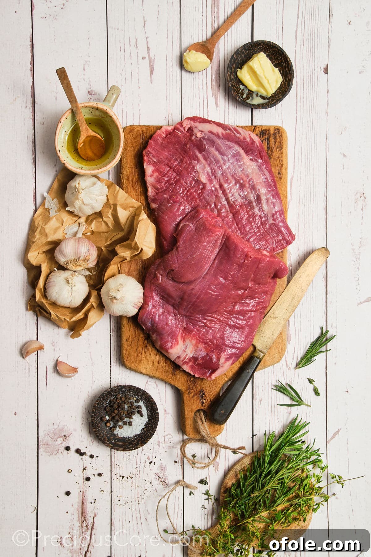 Ingredients for pan seared flank steak laid out, including steak, butter, garlic, and fresh herbs.