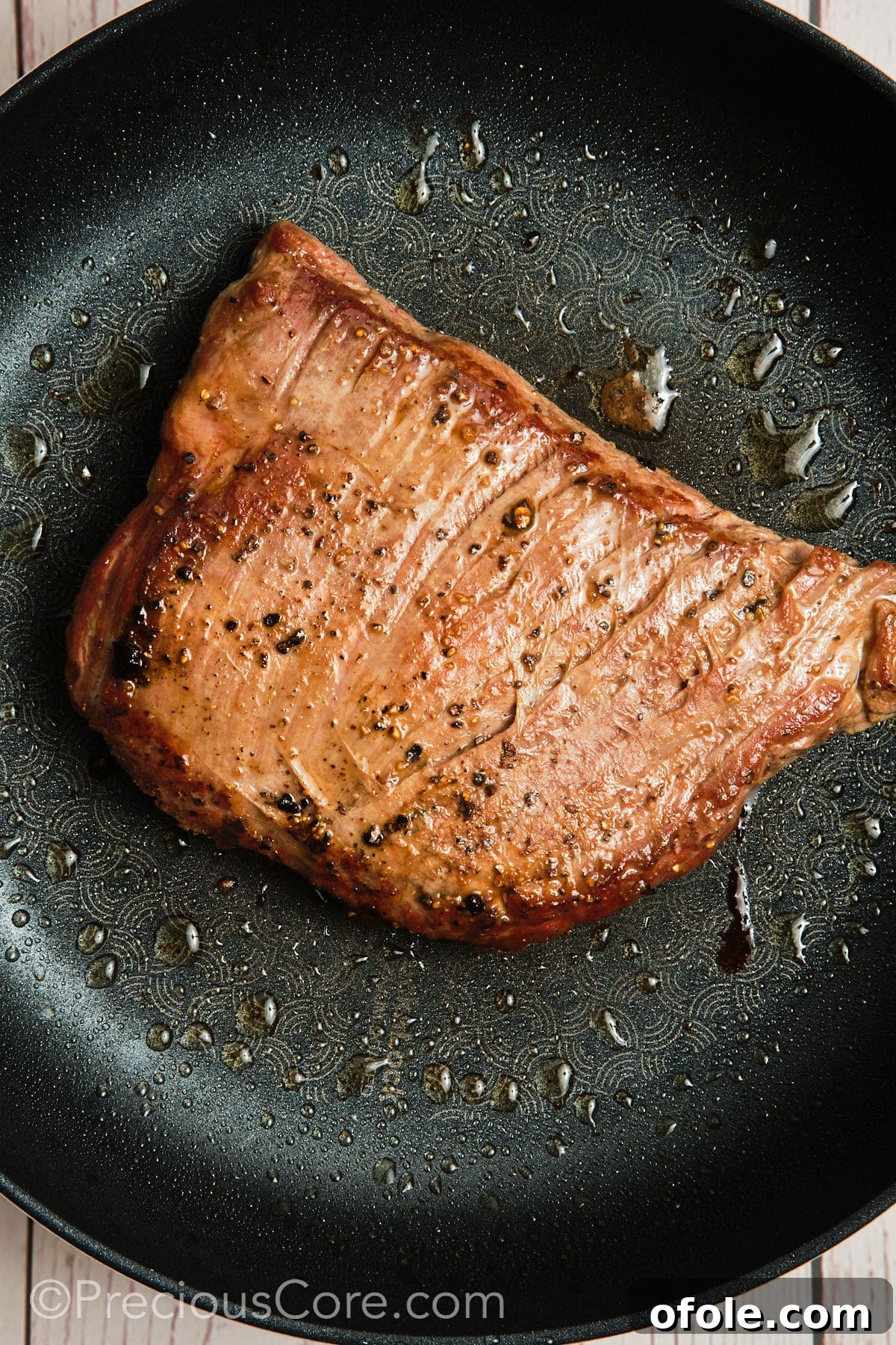 Searing a piece of flank steak in a hot cast iron skillet to develop a crispy crust.
