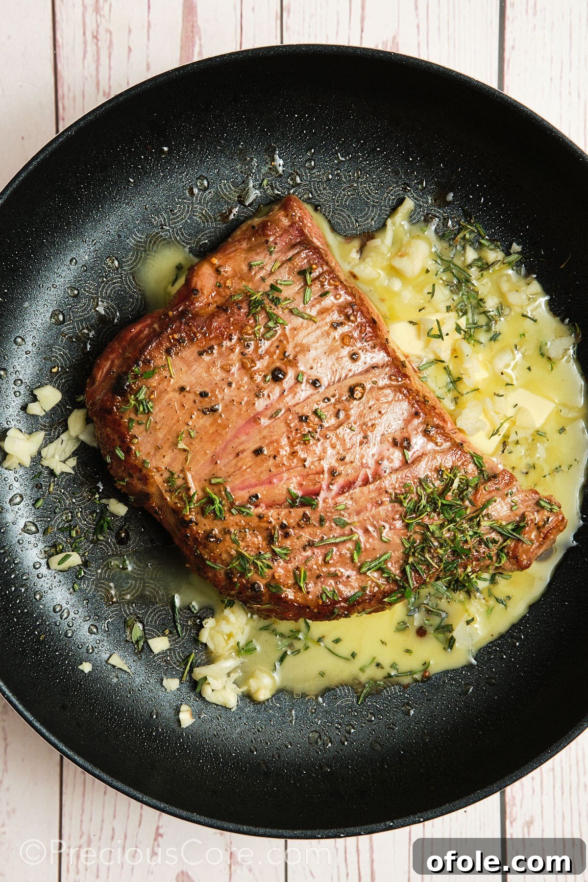 Butter melting in the pan alongside the searing steak, preparing for herb infusion.