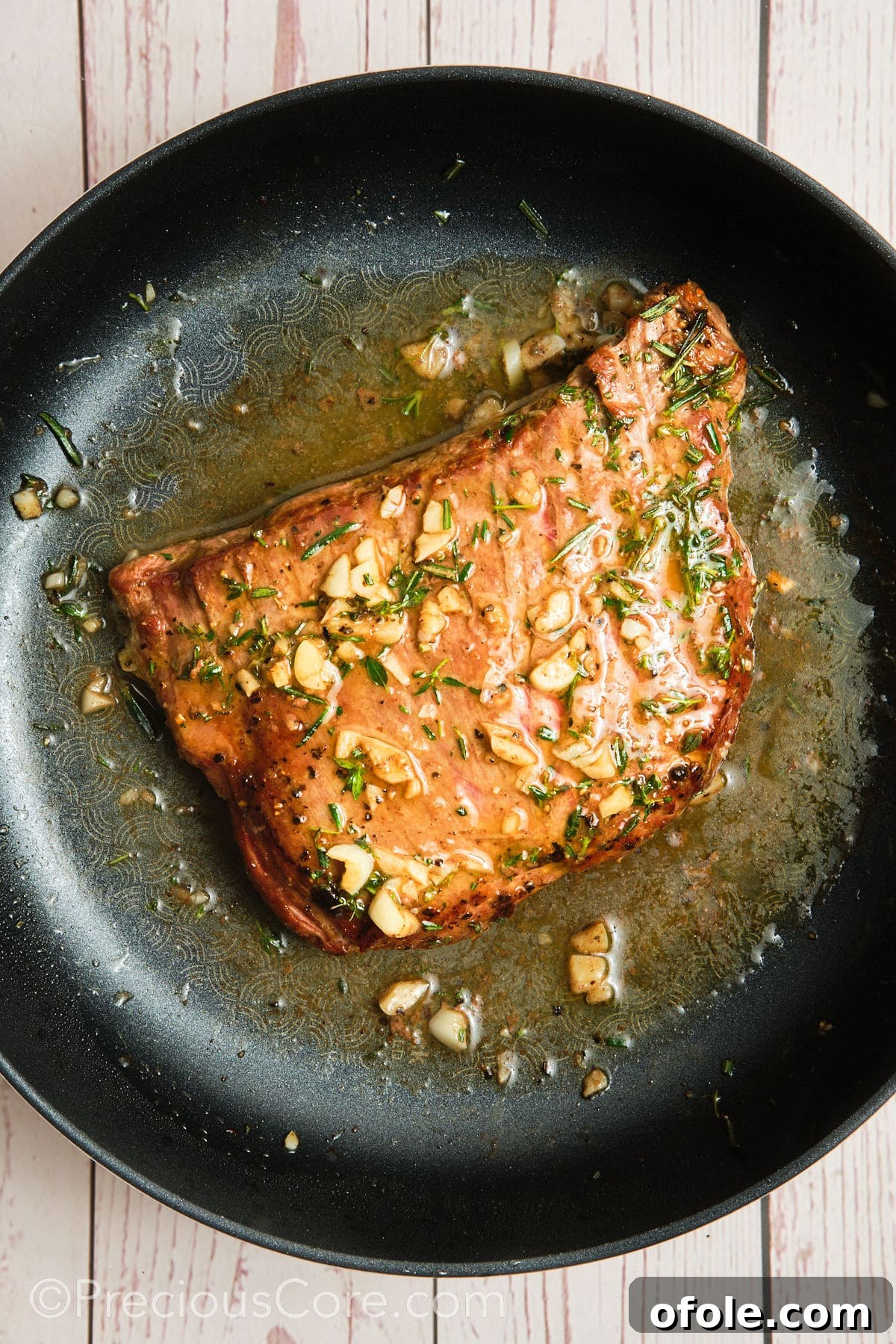 Pan seared flank steak being basted with a fragrant garlic herb butter sauce.