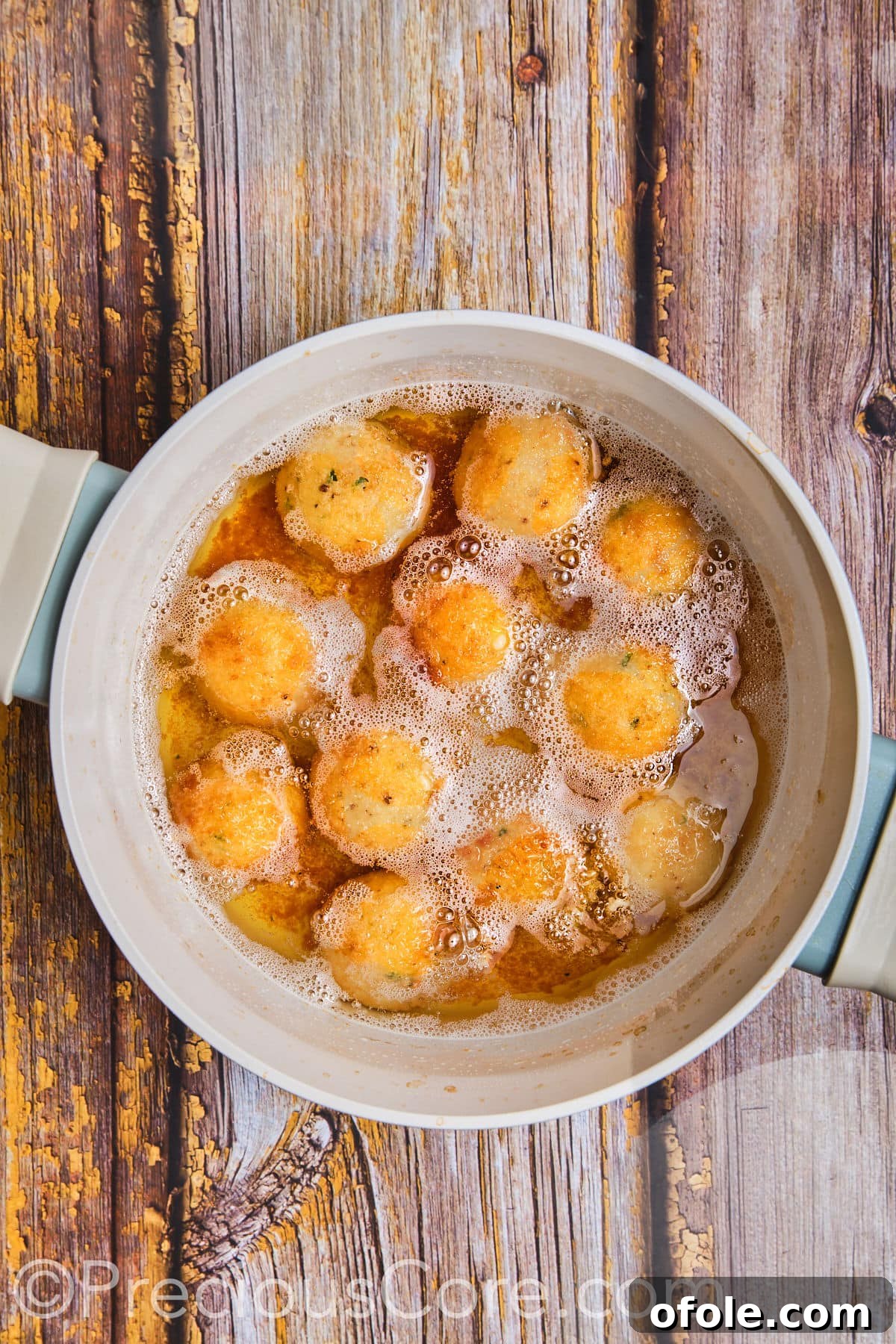 Potato cheese balls being deep-fried in hot oil, turning golden.