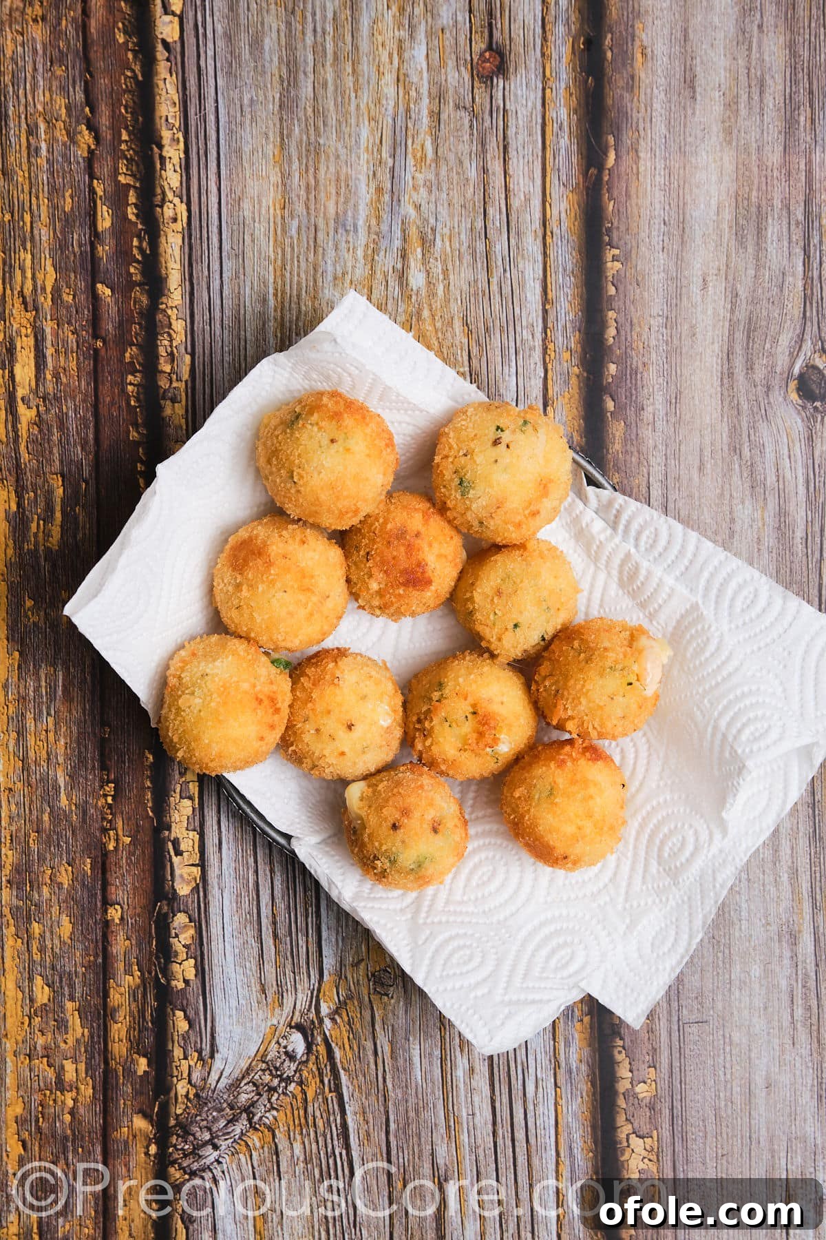 Freshly fried cheesy potato balls resting on paper towels to drain excess oil.