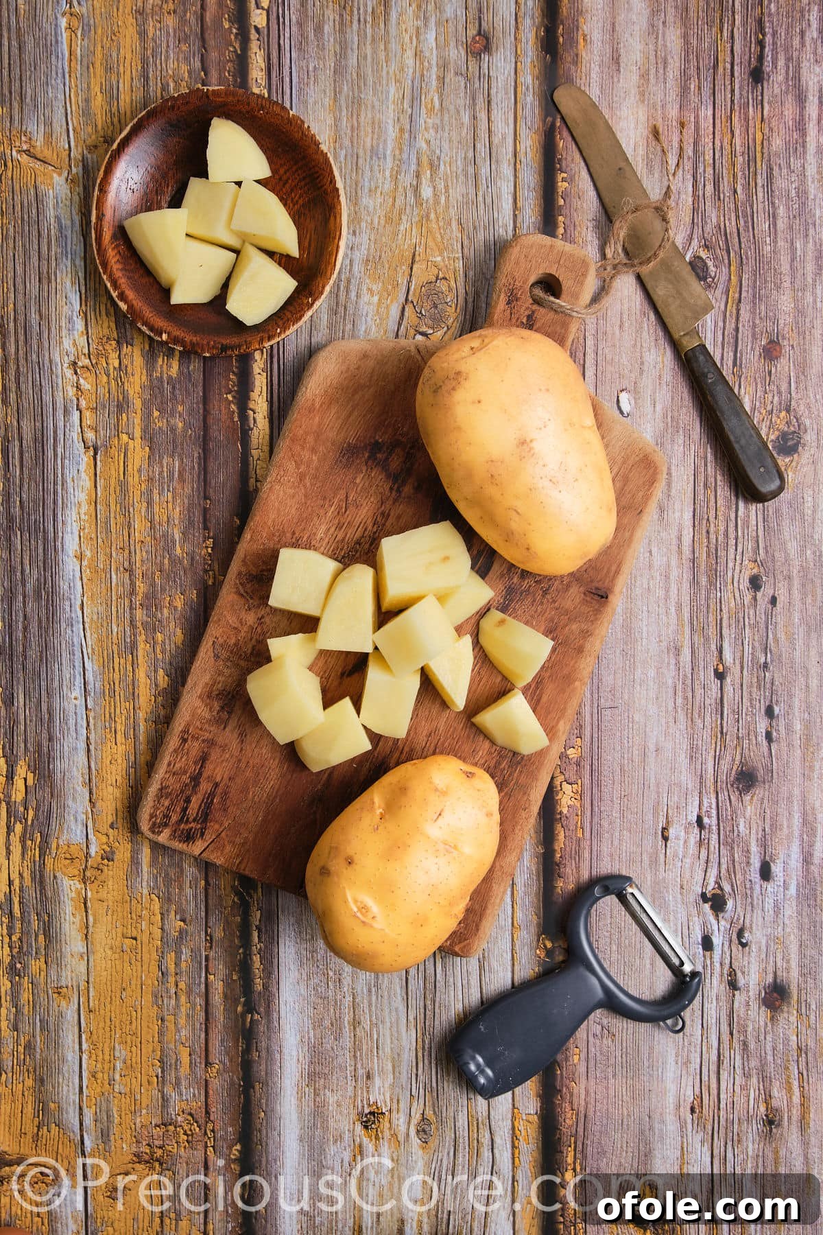 Peeling and cutting potatoes on a wooden chopping board for the recipe.