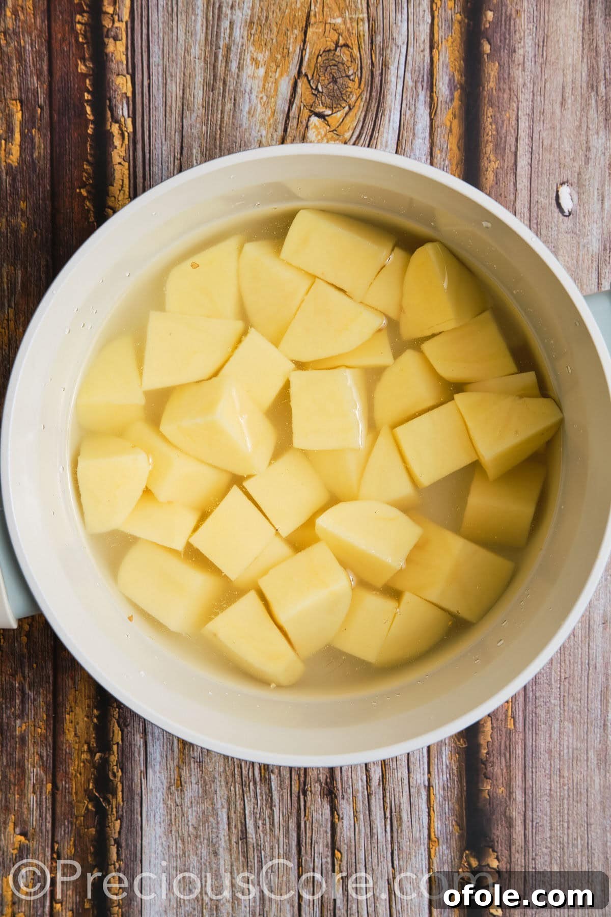 Cut potatoes submerged in cold water in a pot, ready for boiling.