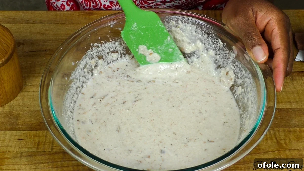 Mixing ground crayfish, pepper, and seasoning into the egusi paste, ensuring even distribution of flavors