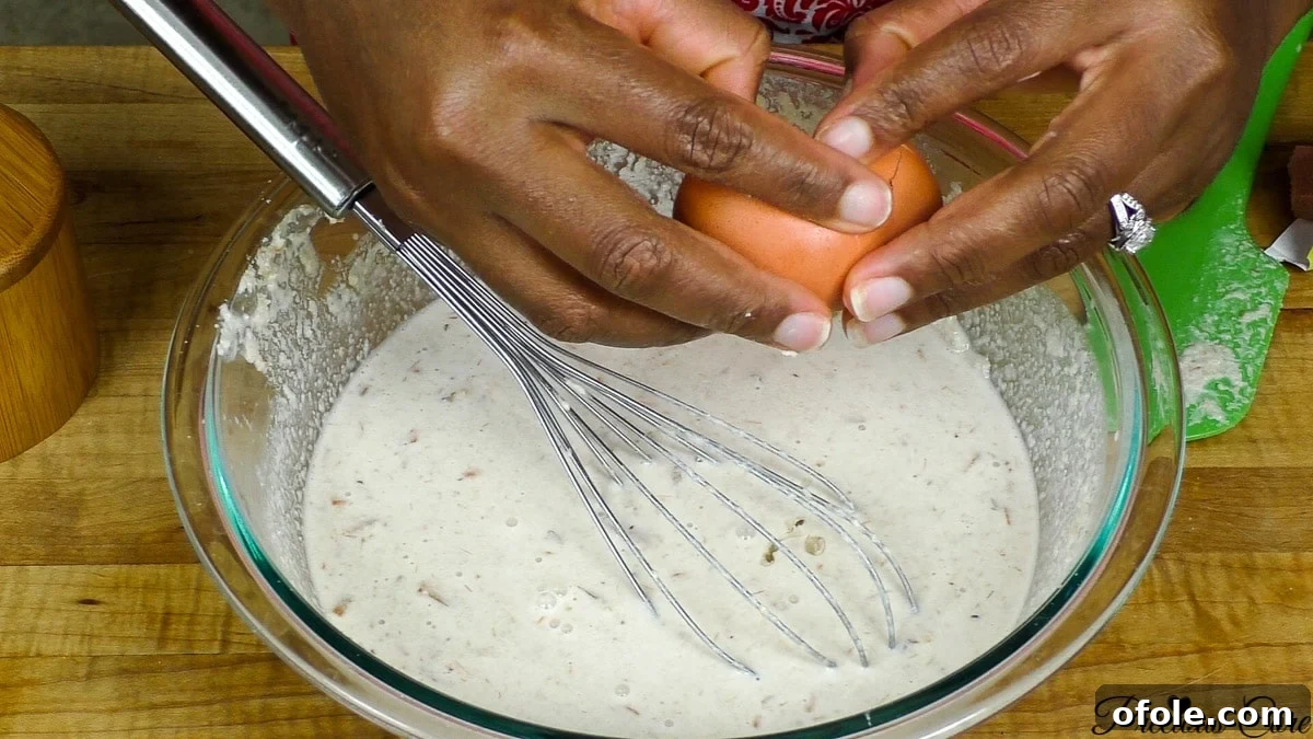 Adding water gradually to the egusi mixture to achieve a smooth and consistent paste