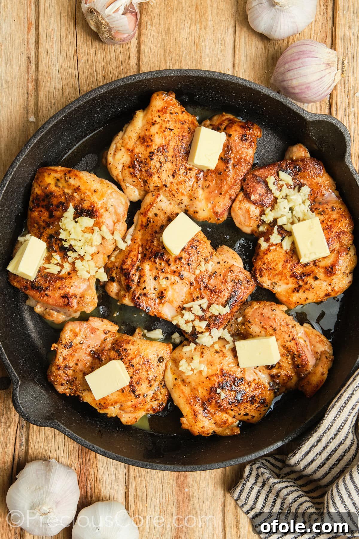 Juicy Skillet Chicken Thighs 14 Cubed butter and minced garlic being added to the hot skillet around the seared chicken thighs.