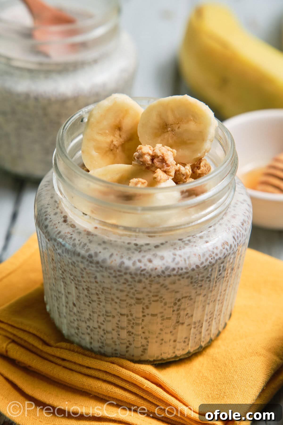 Close-up of a jar of creamy banana chia pudding, topped with fresh banana slices and walnuts.