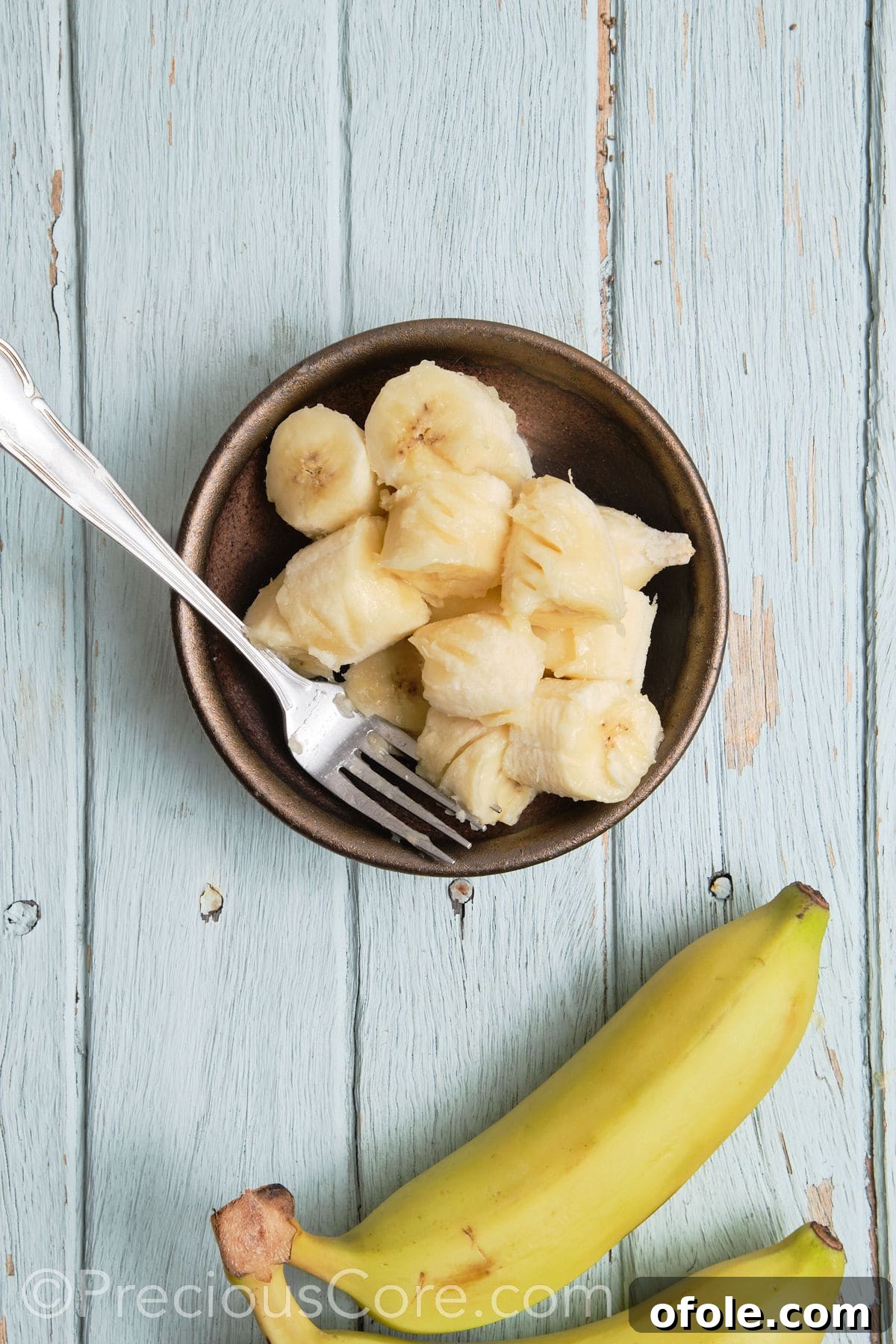 Mashing fresh bananas in a bowl with a fork.