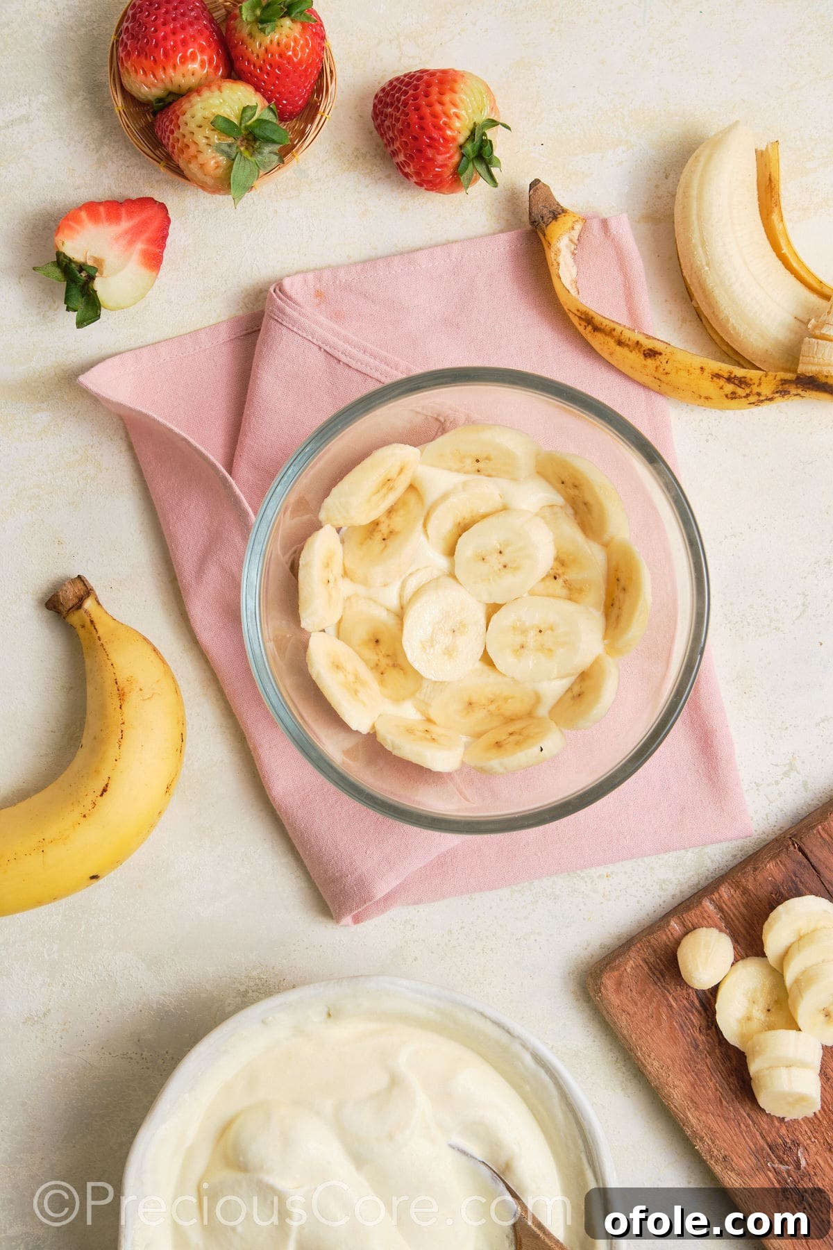 Dreamy Strawberry Banana Pudding 12 Slices of ripe bananas being gently placed over a layer of pudding in a glass bowl, forming an even layer.