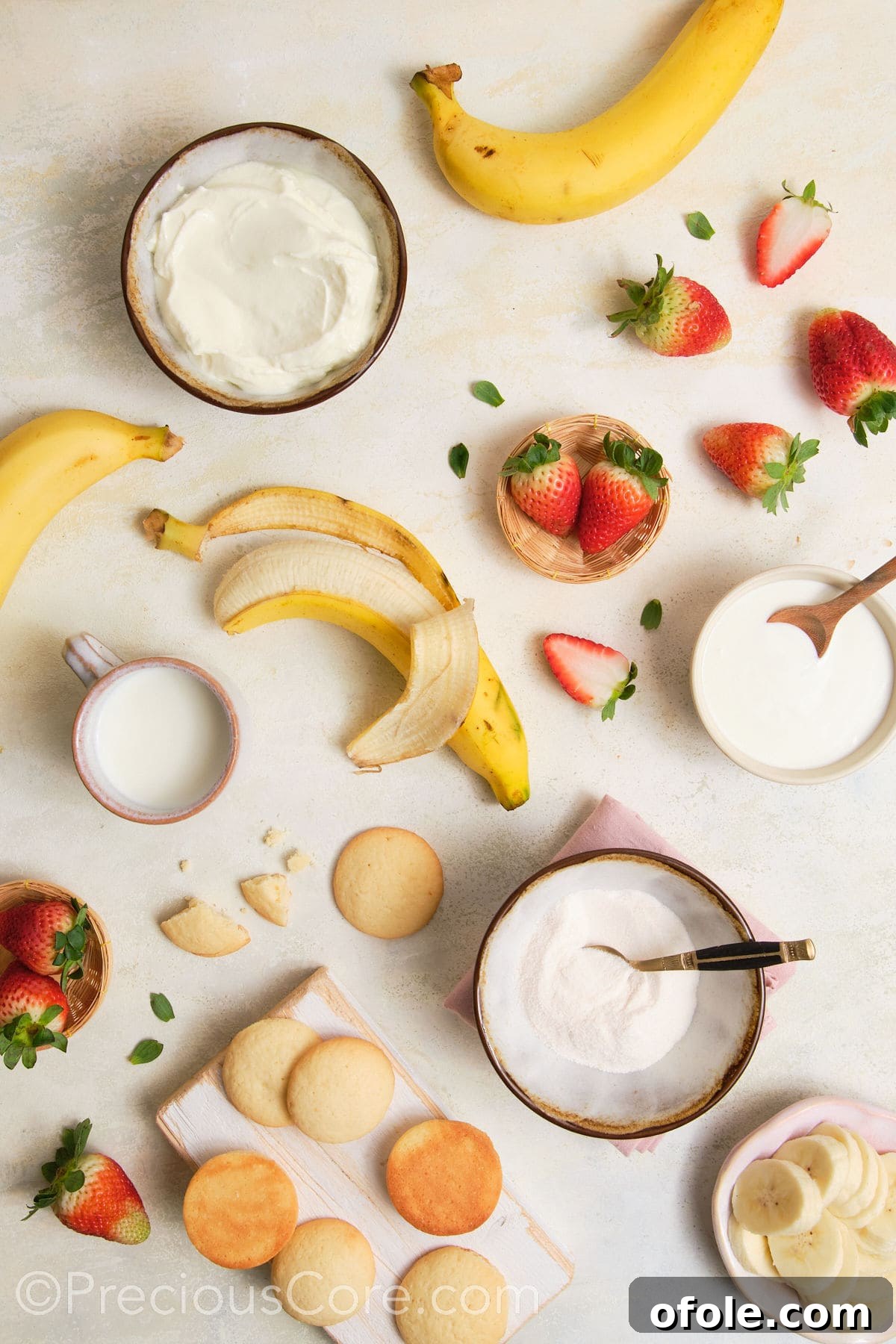 Dreamy Strawberry Banana Pudding 5 A collection of ingredients laid out, including fresh bananas, strawberries, a container of plain Greek yogurt, milk, instant pudding mix, and vanilla wafer cookies.