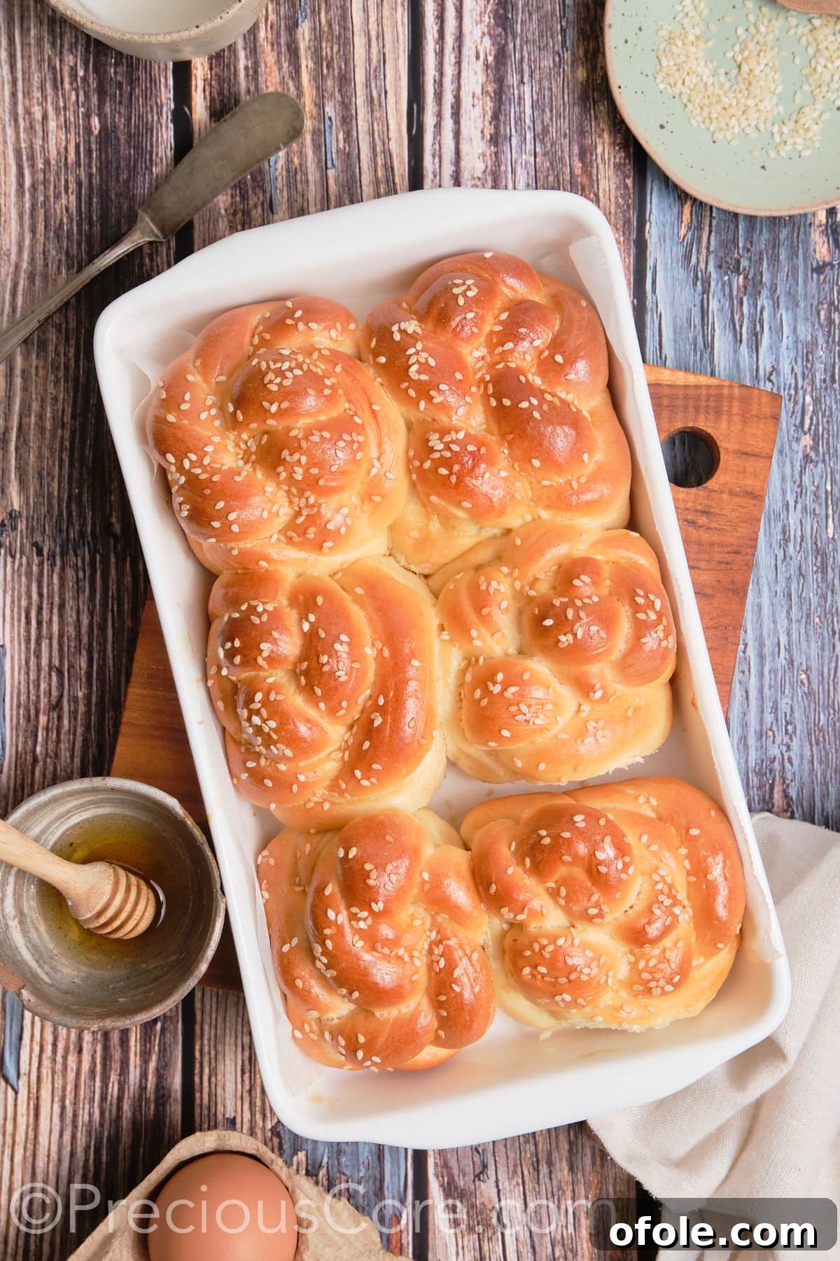 A close-up of beautifully baked challah twists, glistening with egg wash and sesame seeds.