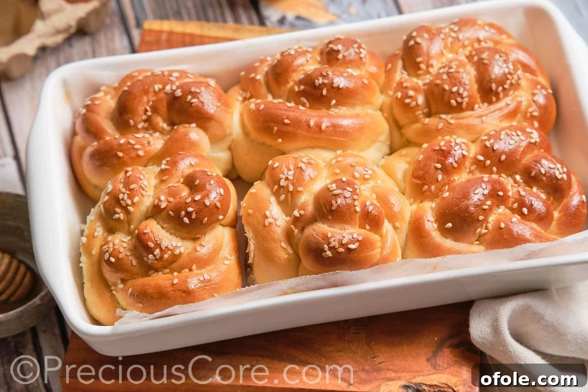 A landscape view of several golden challah dinner rolls, fresh from the oven.