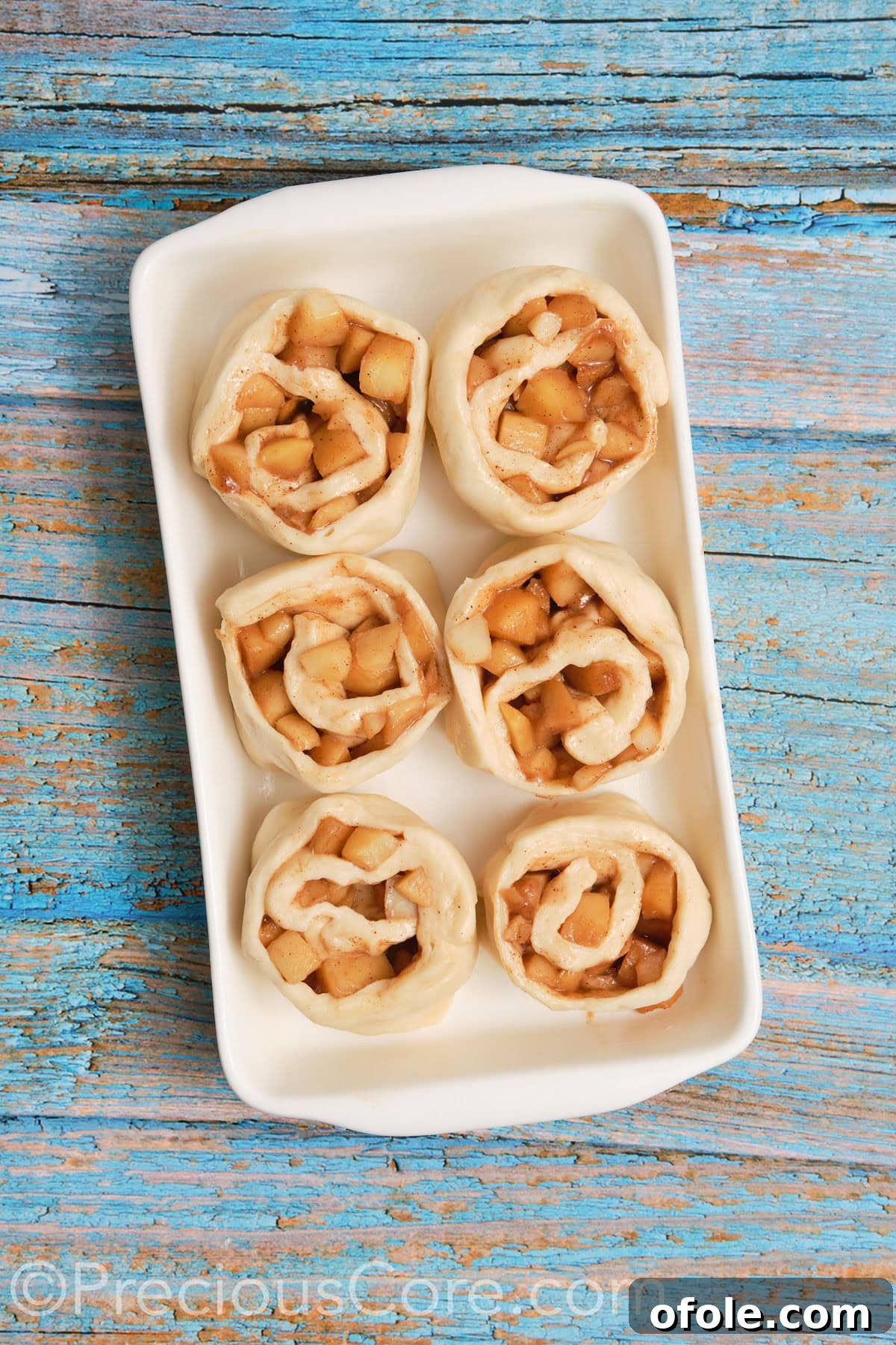 Neatly arranged apple cinnamon rolls placed into a buttered casserole dish, ready for their second rise.