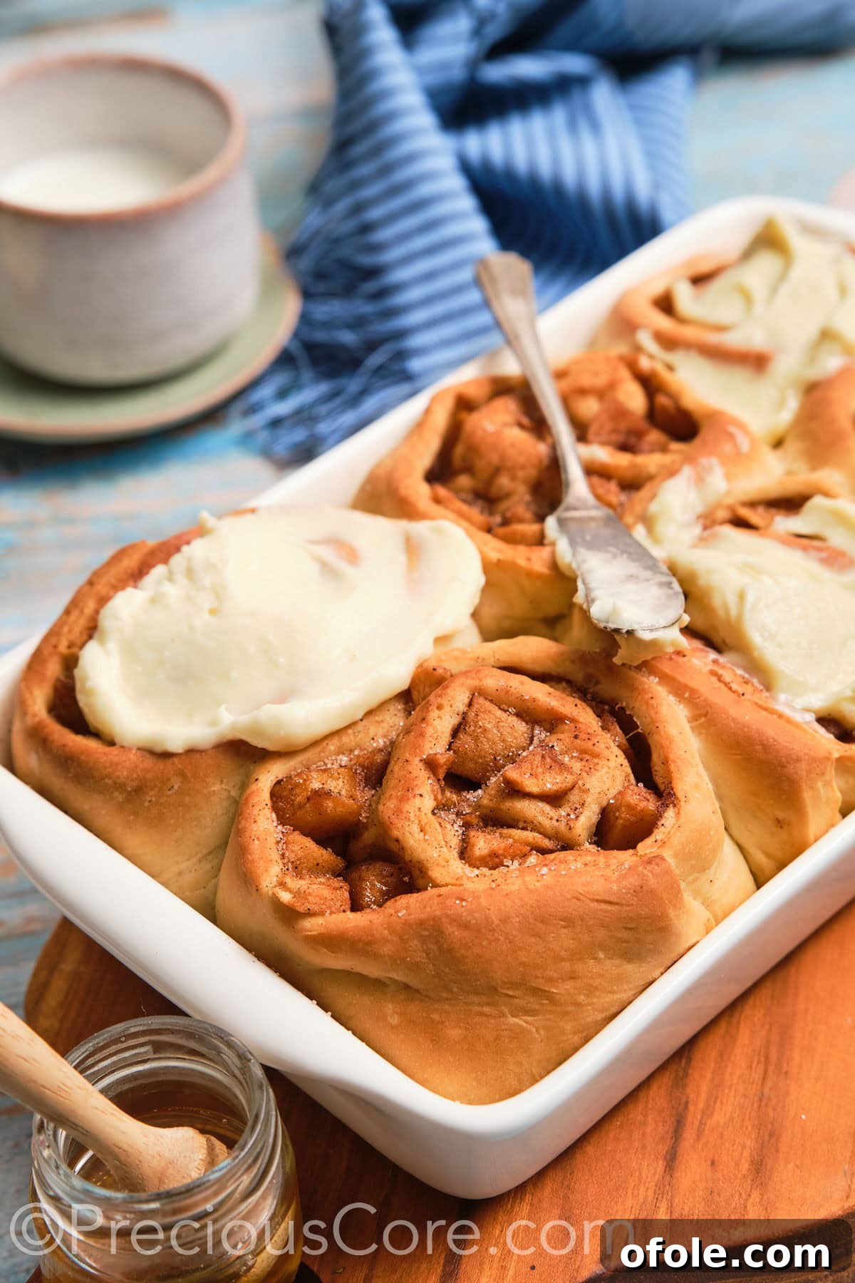 Close-up shot revealing the tender dough and rich apple pie filling inside a sliced cinnamon roll, topped with melting cream cheese frosting.