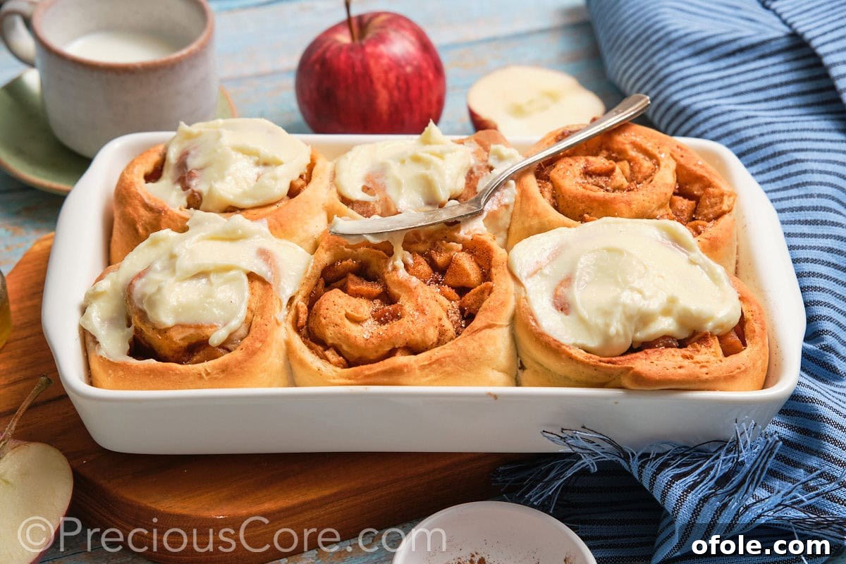 Six perfectly baked and frosted apple cinnamon rolls arranged in a ceramic baking dish, ready to be served.