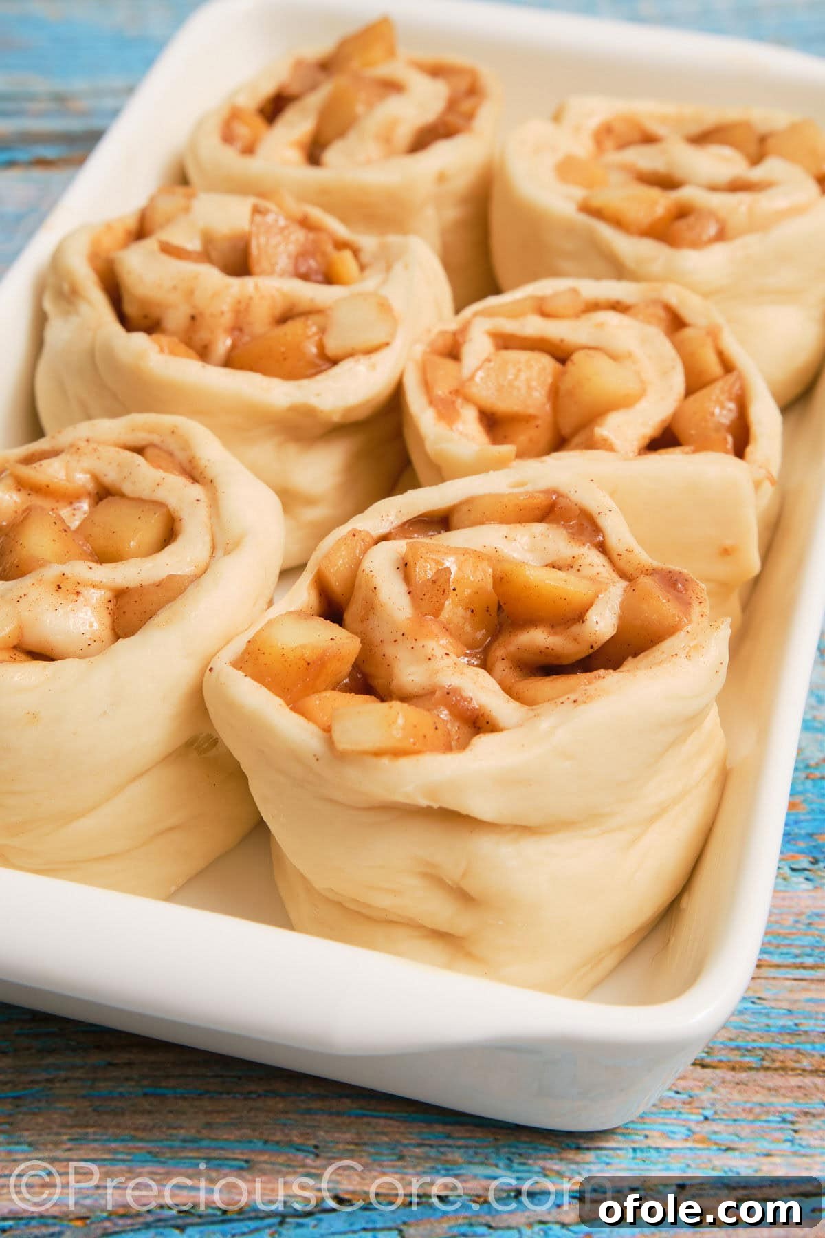 Close-up of fluffy dough generously filled with warm, spiced apple pie filling, rolled and ready for slicing.