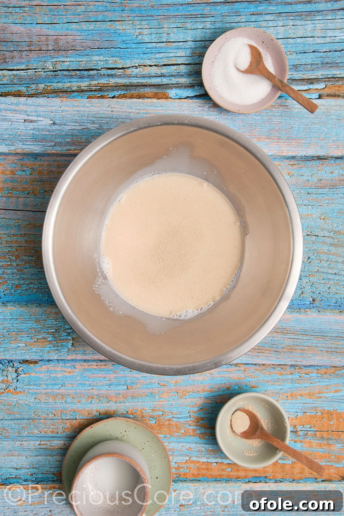 Yeast proofing in warm milk and a touch of sugar in a mixing bowl, showing a foamy top layer.