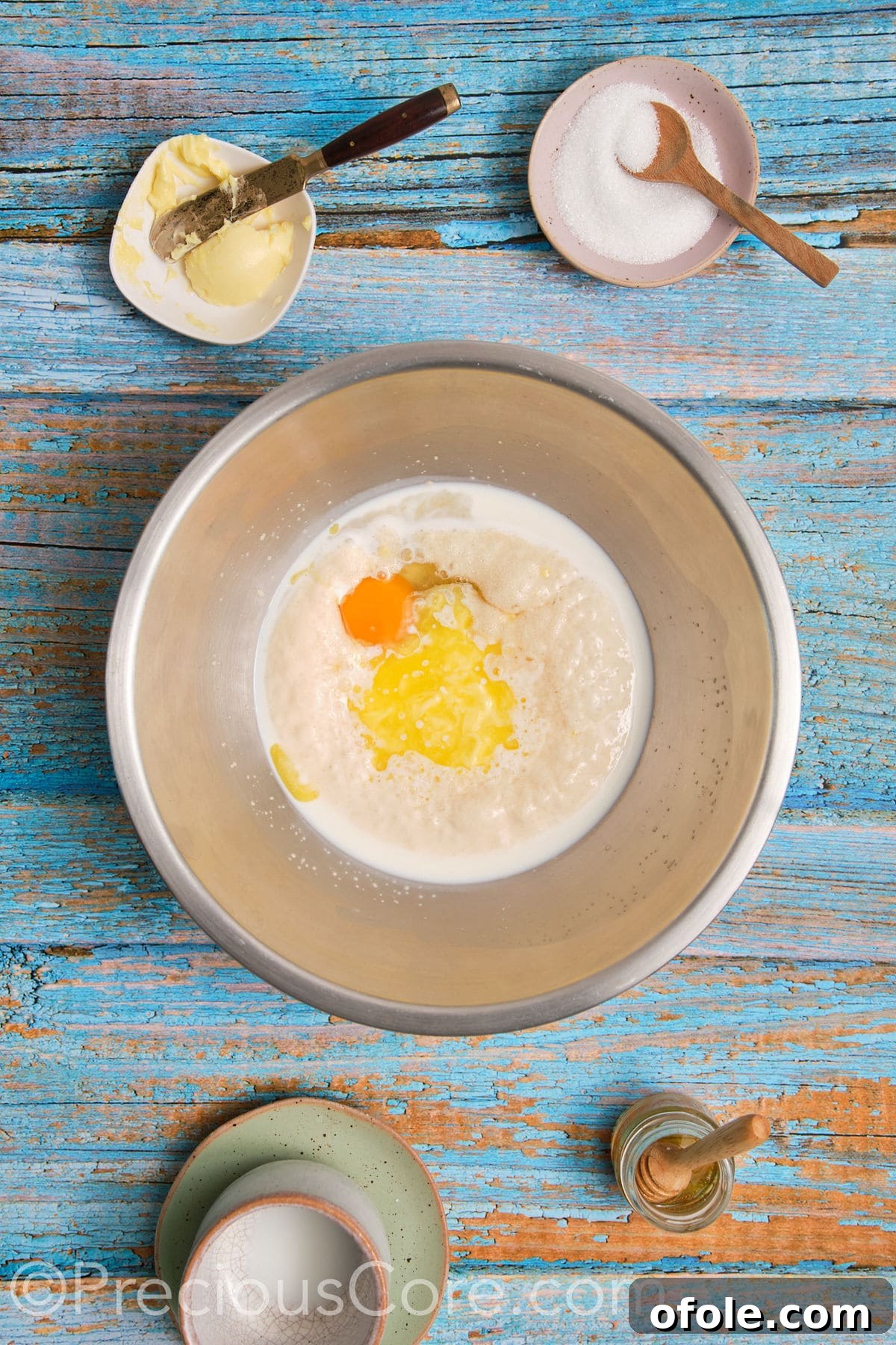 Egg and melted butter being added to the proofed milk and yeast mixture in a bowl.