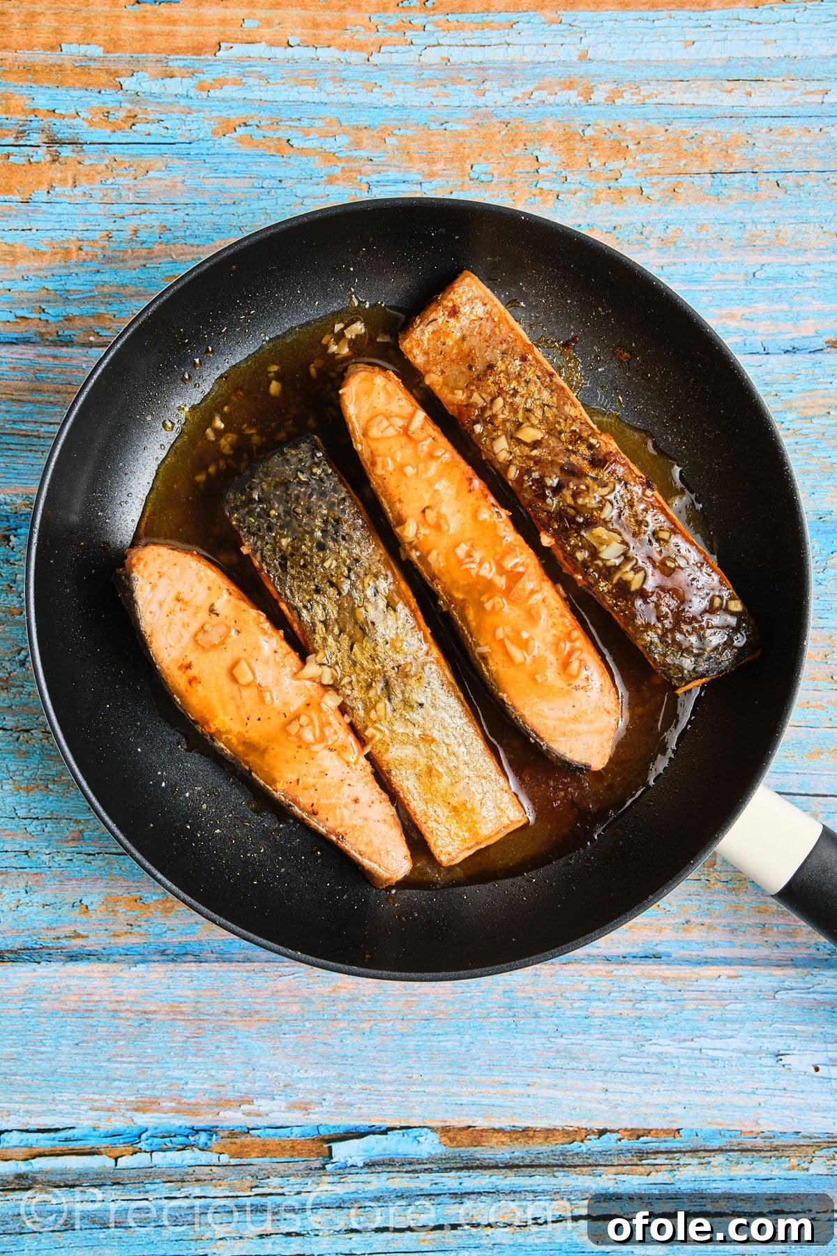 Salmon in skillet simmering in honey butter sauce.