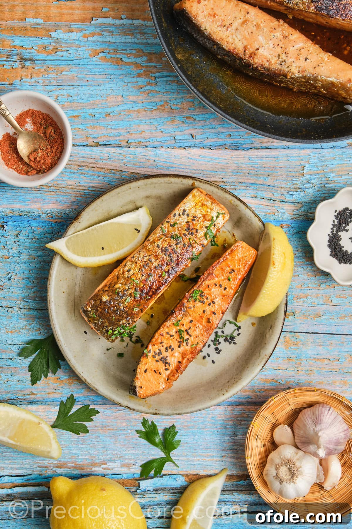 Garnished salmon with chopped parsley, lemon wedges, and black sesame seeds.