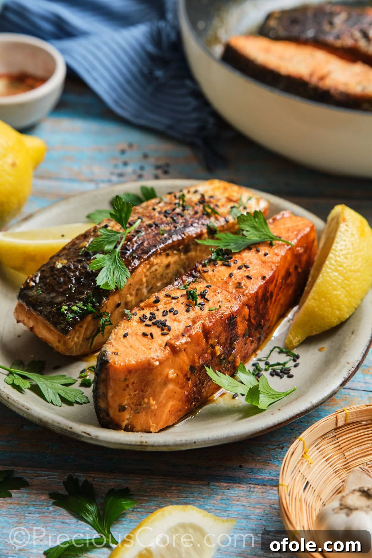 Two cooked salmon fillets garnished with black sesame seeds and parsley.
