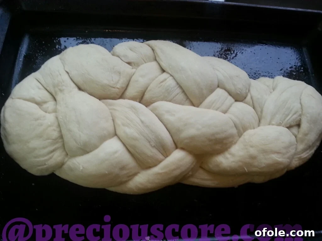 Raw Challah bread dough being braided on a baking sheet.