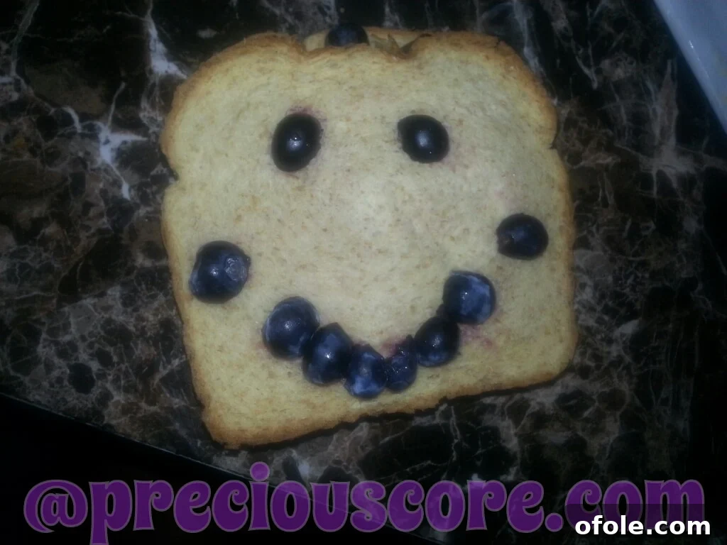 A child's creative breakfast with blueberries and bread meticulously arranged to form a cheerful face.