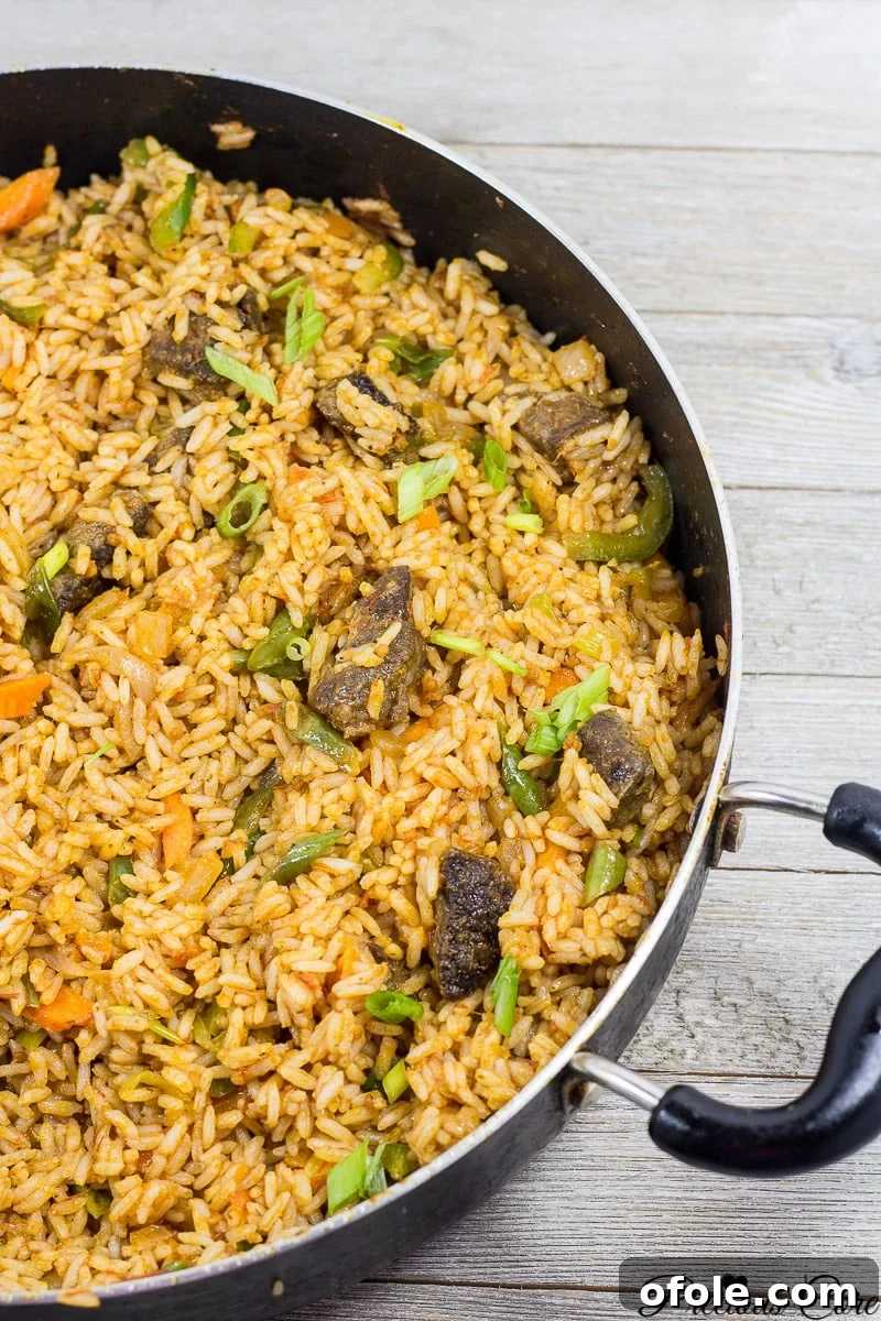 Cameroonian Jollof Rice simmering in a wide pan, showcasing its rich red color and fluffy texture.