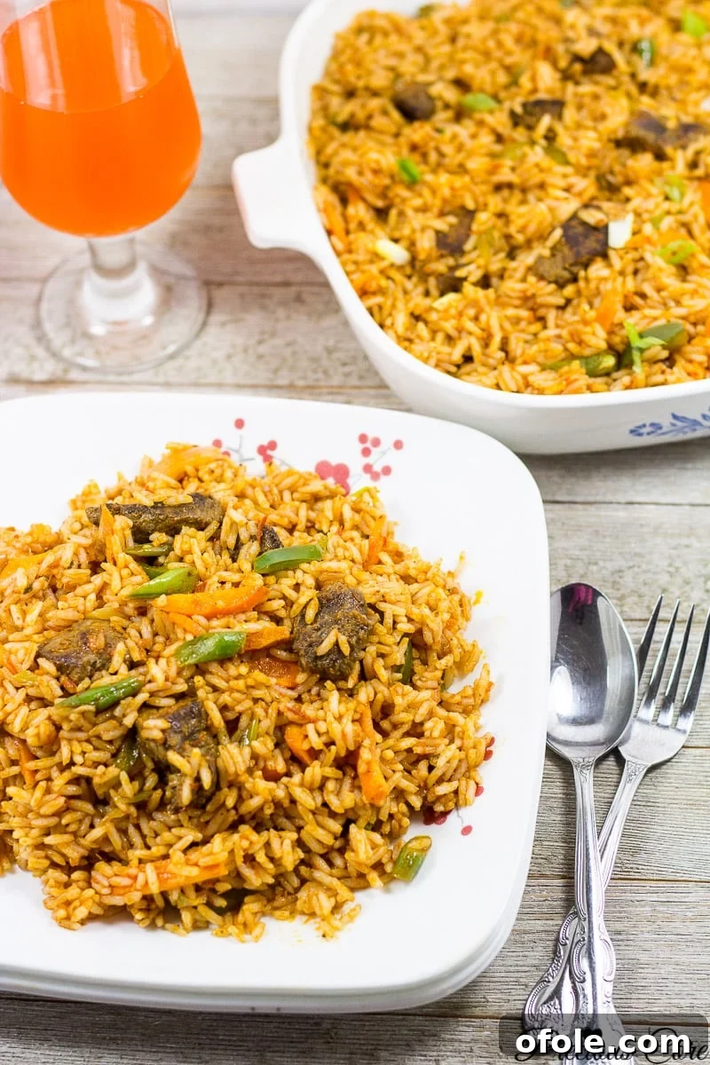 A plate of Jollof Rice with chicken and plantains, served with cutlery, showcasing a complete and appealing meal.