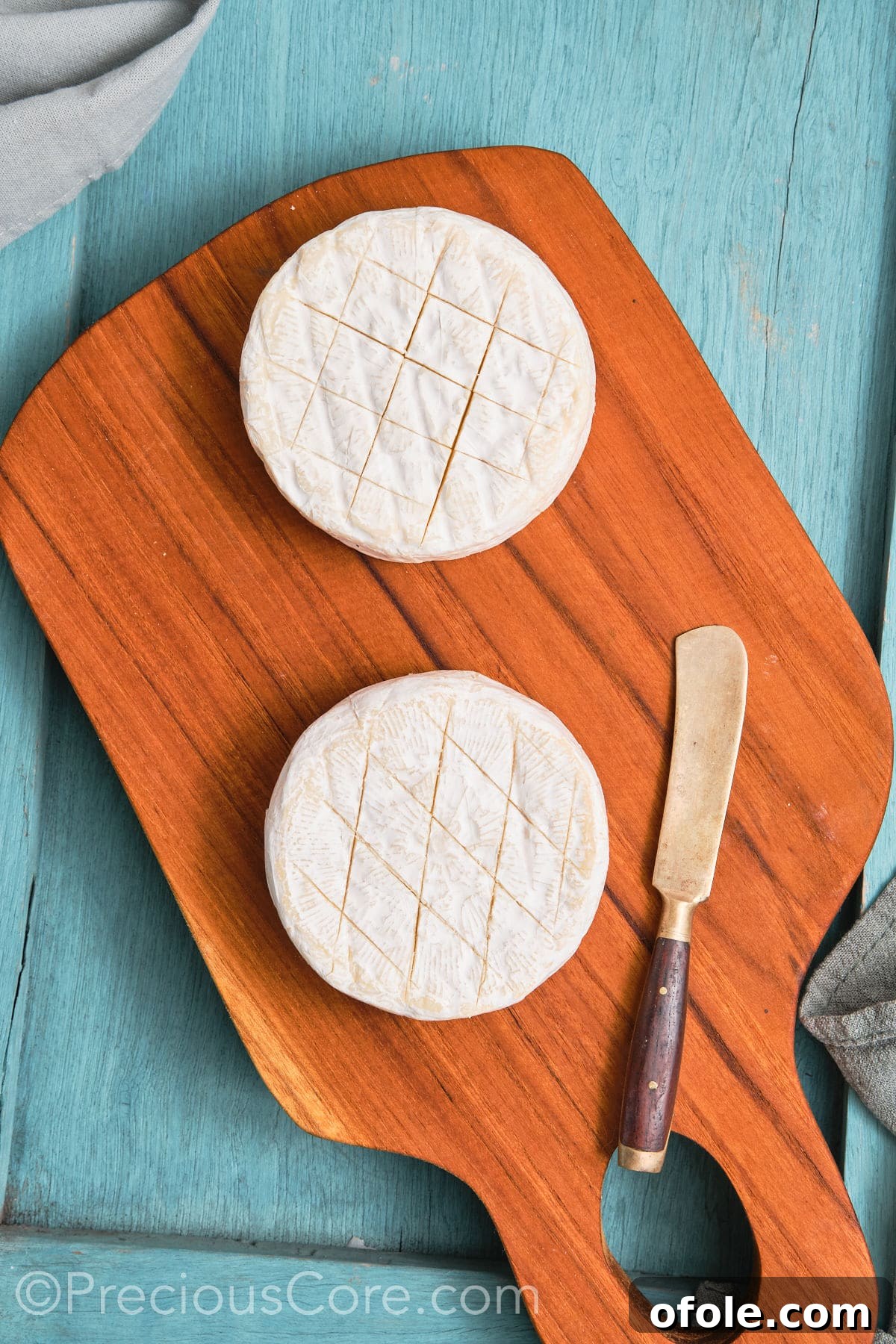 Two rounds of brie cheese, expertly scored in a criss-cross pattern, ready for topping.