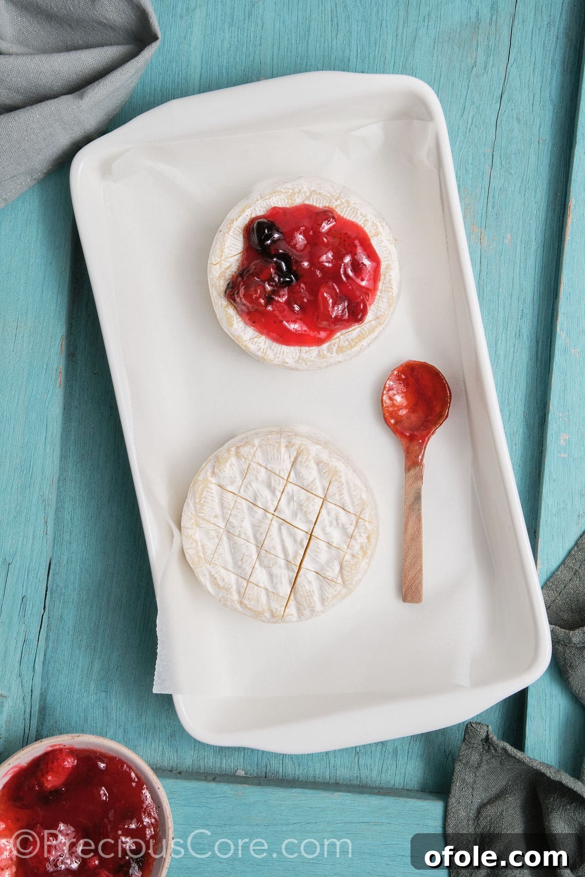 Brie rounds transferred to a baking dish and generously topped with preserves, before baking.