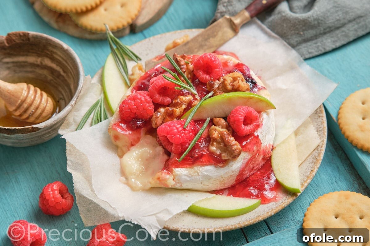 A stunning round baked brie with fruit preserves, garnished with fresh berries and herbs.