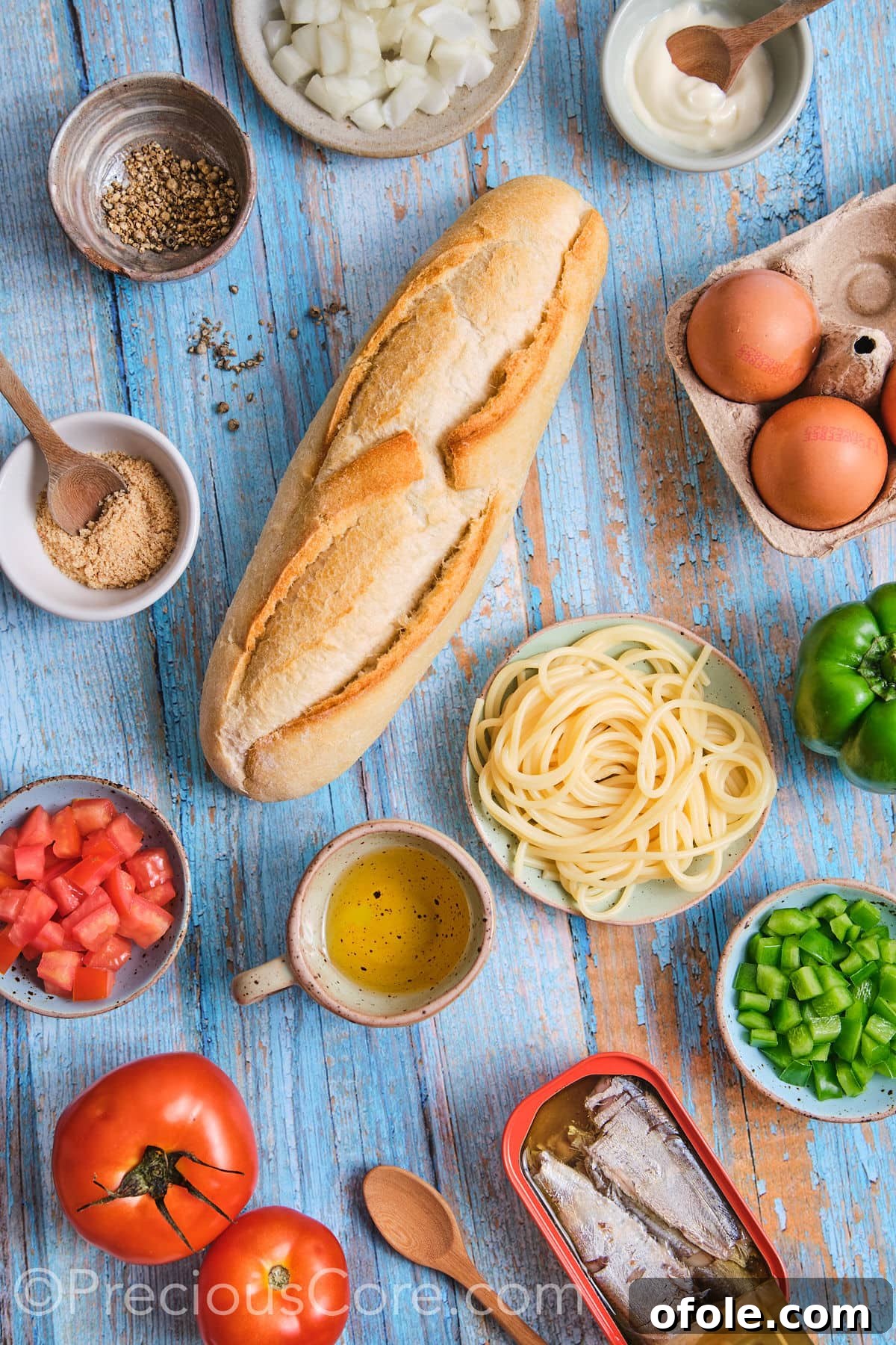 Cameroon's Signature Spaghetti Omelette Sandwich 4 A collection of fresh ingredients laid out for homemade spaghetti omelette sandwich, including tomatoes, onions, bell peppers, eggs, spaghetti, and a baguette.