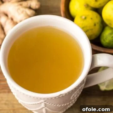 A mug of fresh ginger drink with some ginger slices and key limes on the side