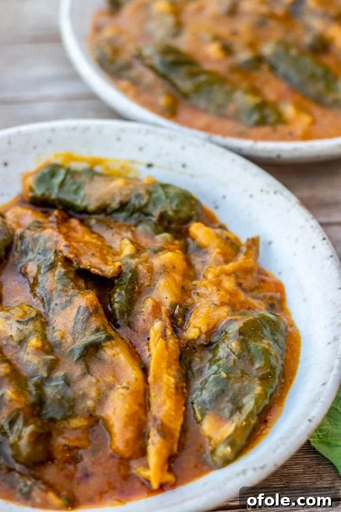 A close-up view of Ekwang served on a plate, highlighting its unique texture, the vibrant green of the wrapping leaves, and the rich orange hue of the stew.