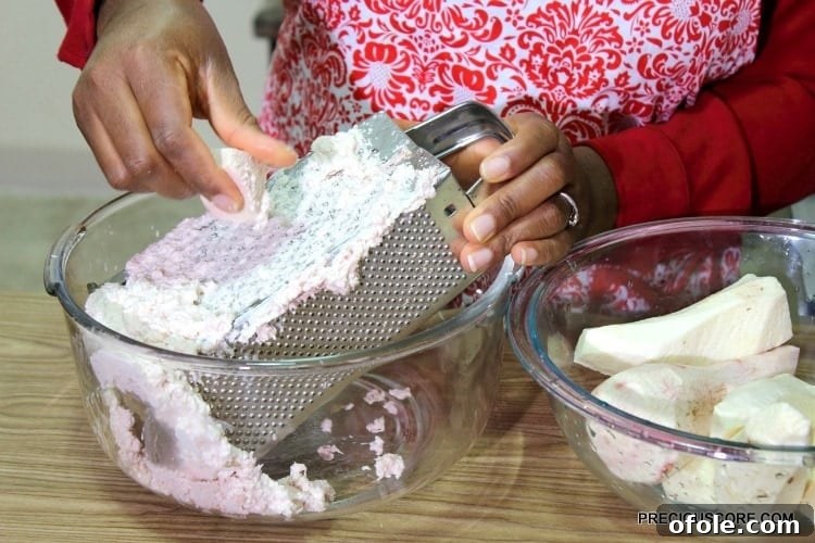 A person expertly grating cocoyams on a traditional box grater, demonstrating the manual process to achieve the ideal paste for Ekwang.