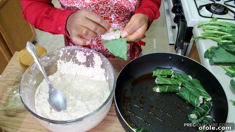 Close-up shot of cocoyam paste being meticulously wrapped in a green leaf, illustrating the technique of creating individual Ekwang parcels.