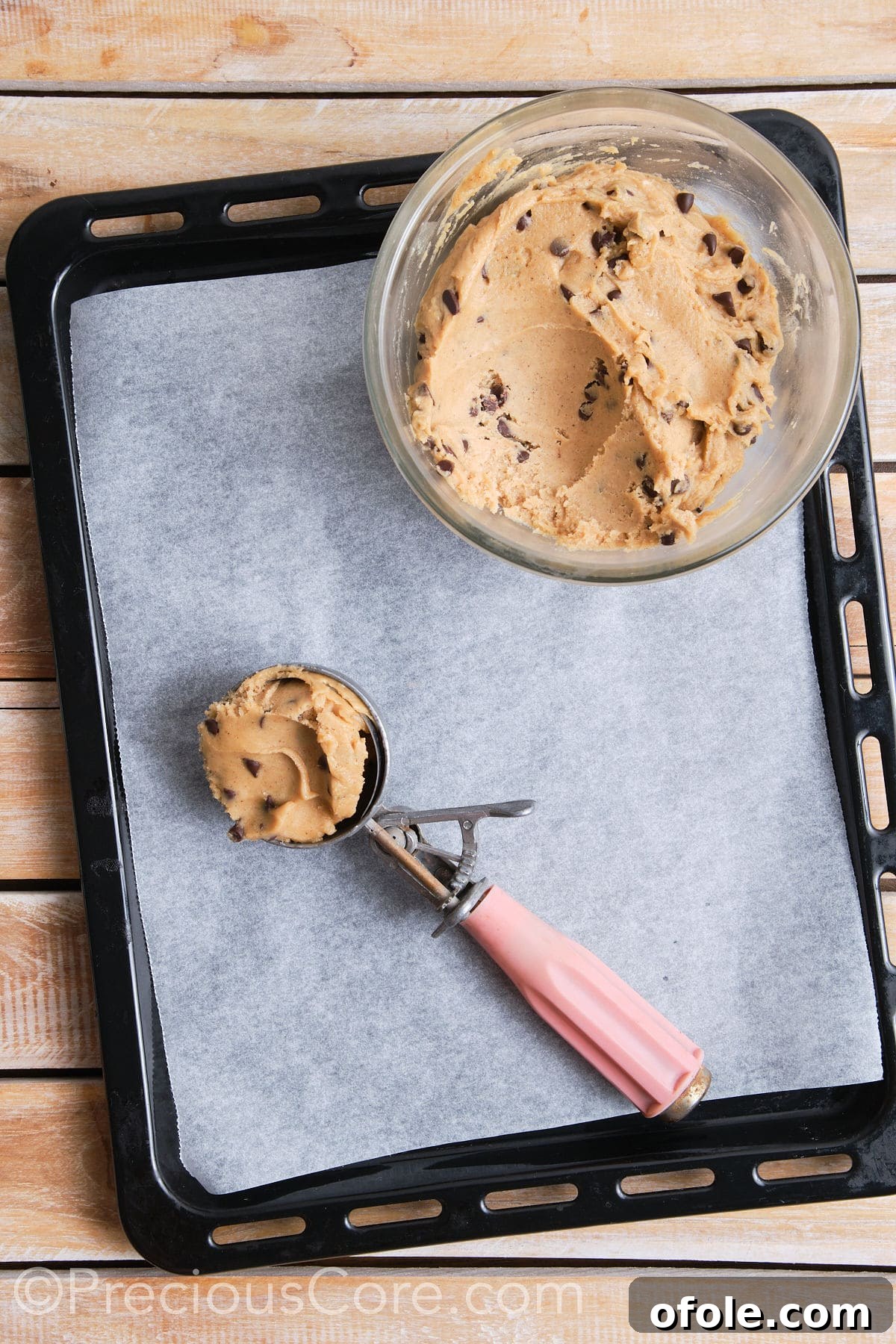 A scoop filled with the cookie dough, placed on a lined baking sheet