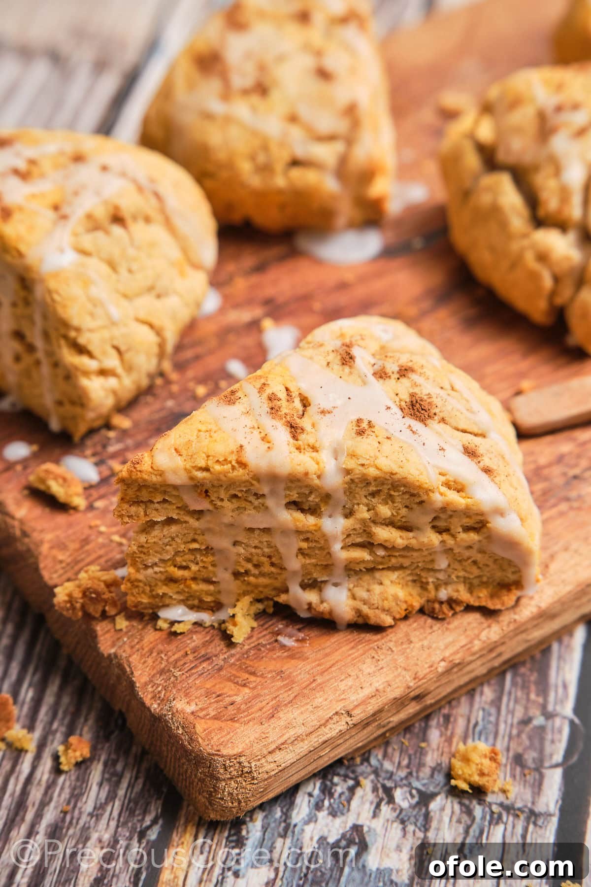 Spiced Sweet Potato Scones 2 A perfectly triangular sweet potato scone with a glistening white glaze drizzled over its golden-brown top, resting on a rustic wooden surface.