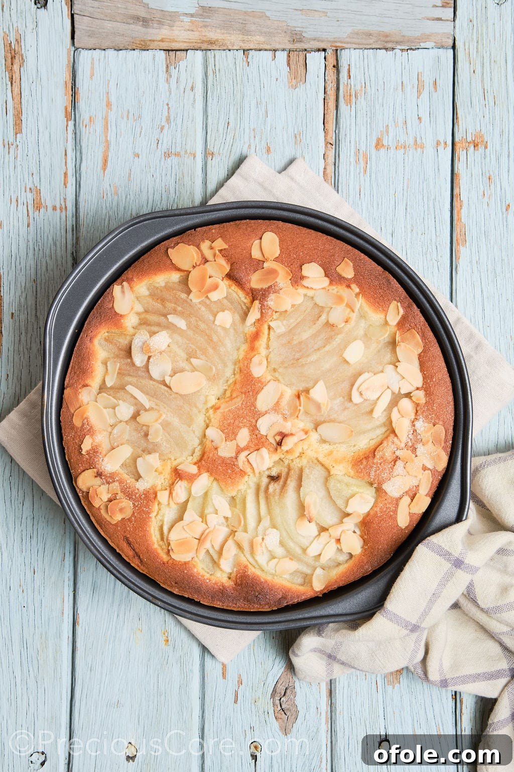 A freshly baked pear and almond cake, golden brown and puffed, just removed from the oven and cooling in its pan.