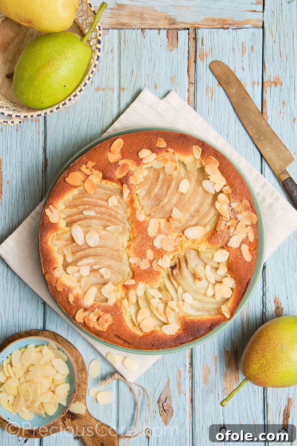 A whole, beautiful almond and pear cake resting on a decorative serving plate, lightly dusted with icing sugar and ready to be sliced.