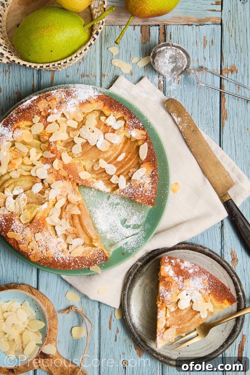 A gorgeous pear and almond cake, beautifully dusted with powdered sugar, sliced and arranged on a serving plate.