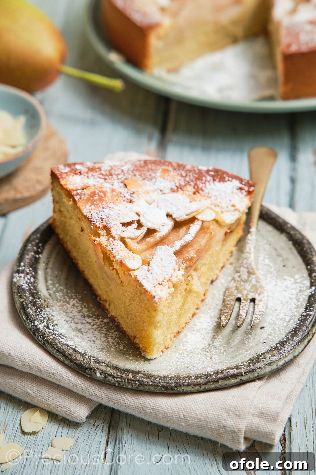 A perfect slice of pear almond cake, elegantly dusted with powdered sugar, resting on a white plate, ready to be enjoyed.