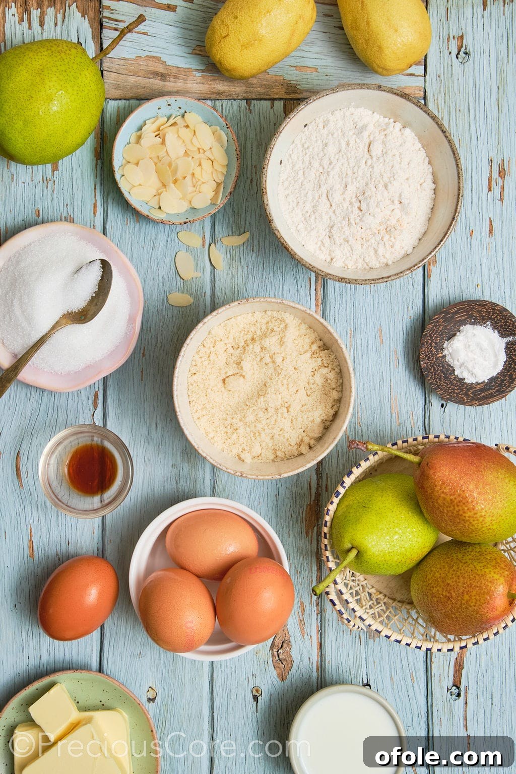 A collection of fresh, high-quality ingredients laid out for the pear almond cake recipe, including pears, butter, eggs, flours, and sugar.