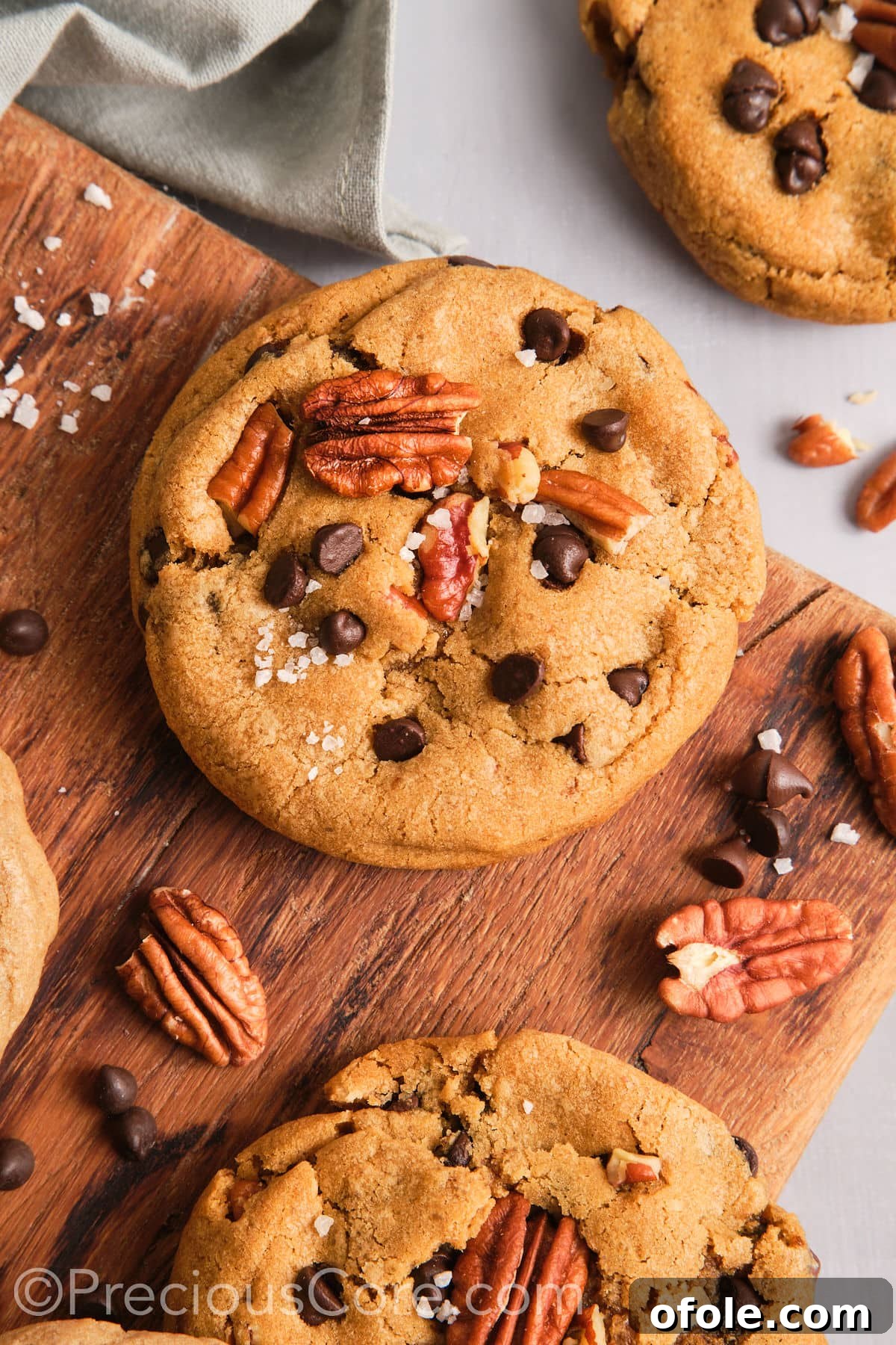 Decadent Brown Butter Pecan Delights 2 Crispy and chewy brown butter pecan cookies on a rustic chopping board, elegantly garnished with flaky sea salt and pecan halves.