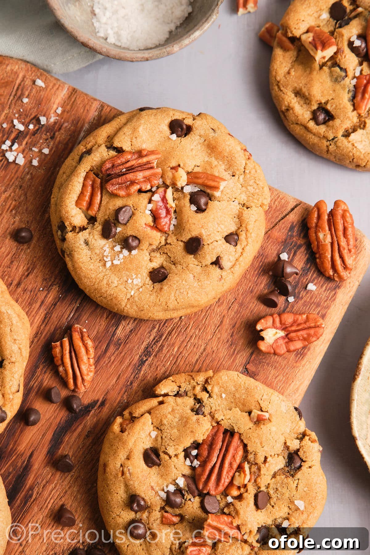 Decadent Brown Butter Pecan Delights 17 Brown butter pecan cookies elegantly sprinkled with flaky sea salt on a dark, textured surface, enhancing their visual appeal.