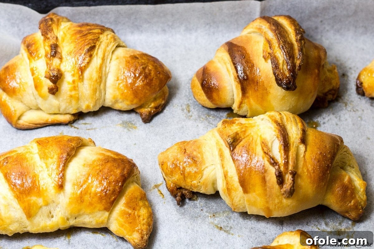 Flavor Friday 2 Freshly baked homemade croissants cooling on parchment paper, showcasing their golden-brown, flaky layers and irresistible texture.